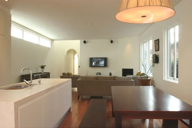 Living room with beige couches, a tree branch decoration, TV, fireplace, wooden table, and large windows in a modern home.