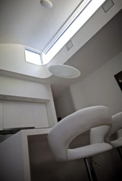 Interior of a modern room with a skylight, white chairs, and minimal decor.