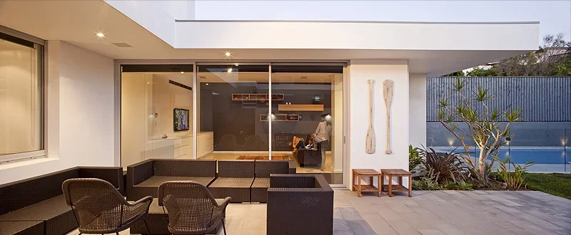 Modern backyard patio with outdoor seating, large glass doors, a pool, and landscaped plants.