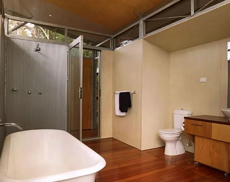 A modern bathroom featuring an open shower area with metal doors, a clawfoot bathtub, a toilet, a wooden vanity with a sink, and a towel hanging on a wall-mounted bar.