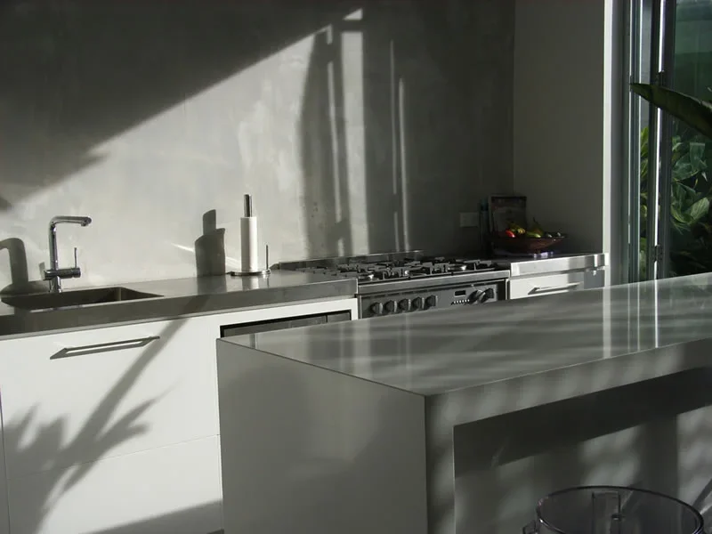 Modern kitchen with white cabinetry, a stainless steel sink, a soap dispenser, a paper towel holder, a gas stove, and a large counter with sunlight casting shadows.