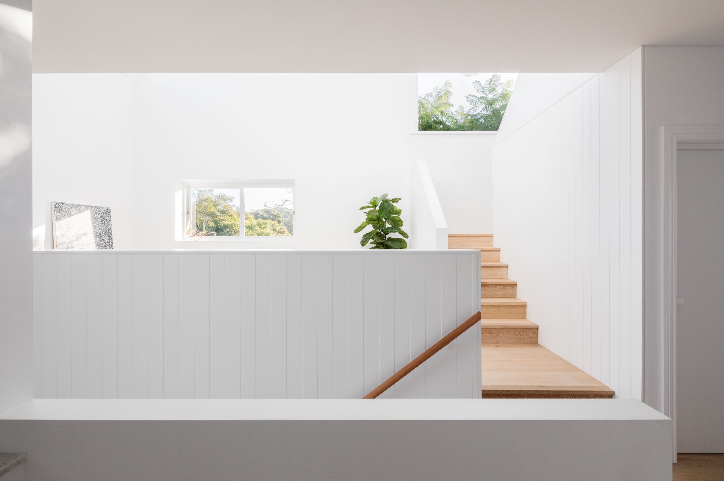 Light-filled stair landing with timber steps, white-lined walls and skylight bringing natural light into the interior.