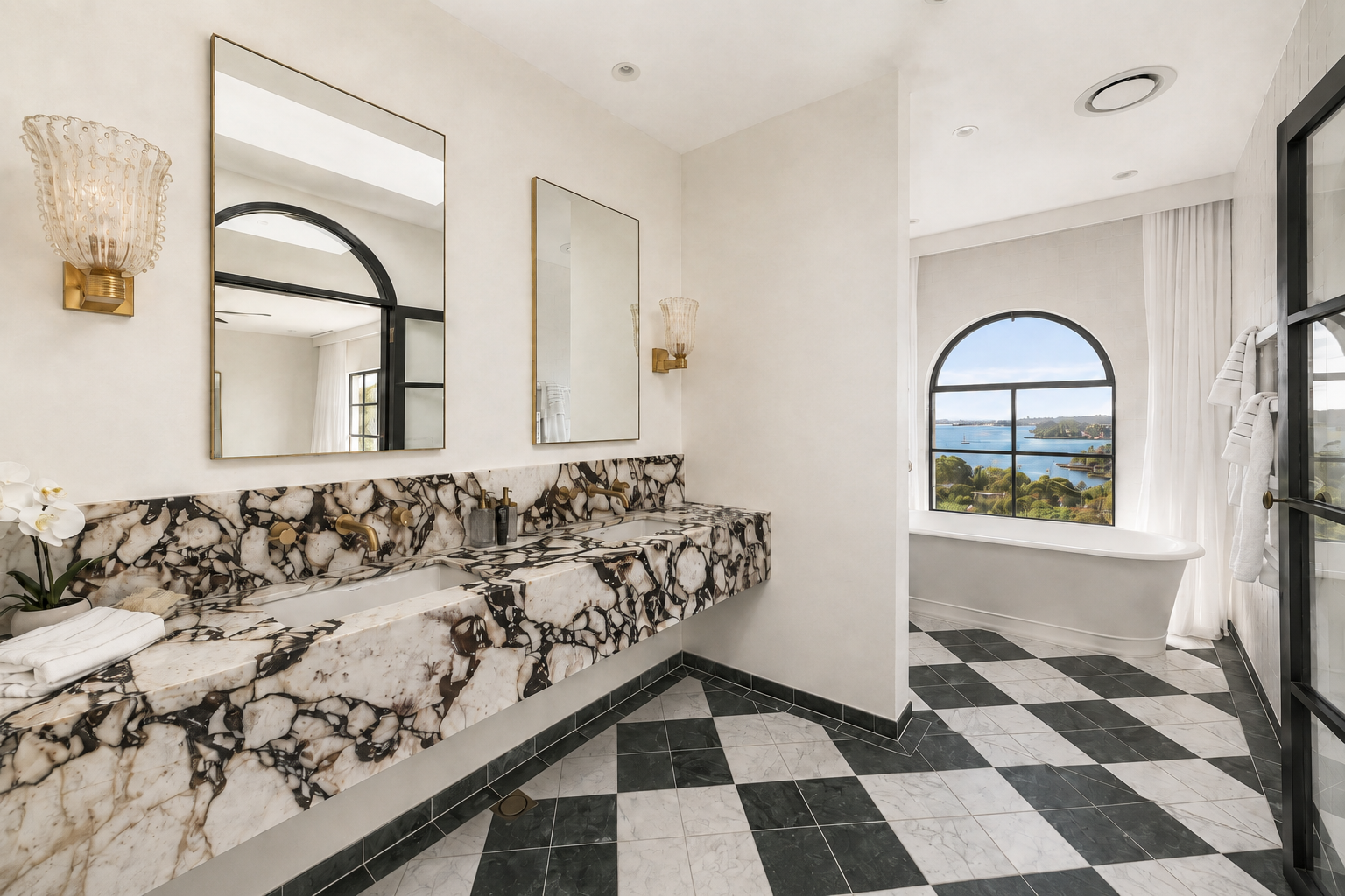 Modern bathroom with black and white checkered floor, a marble double vanity, mirrors, and a large window with a view of water and greenery.
