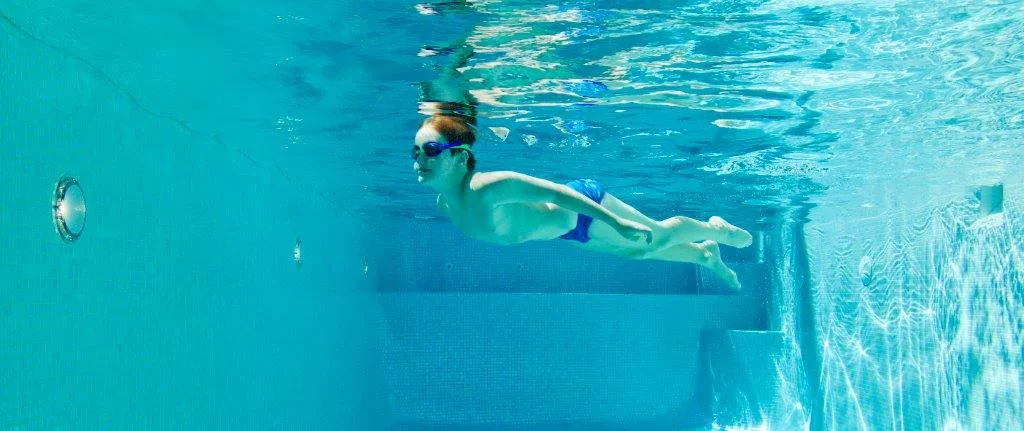 Child swimming underwater in a pool wearing goggles.