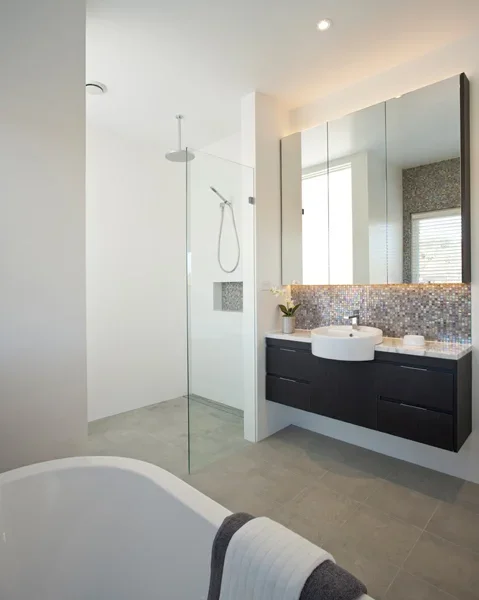 Modern bathroom with a glass-enclosed shower, a dark vanity with a white vessel sink, a large mirror, a potted plant, and a bathtub with a towel draped over it.