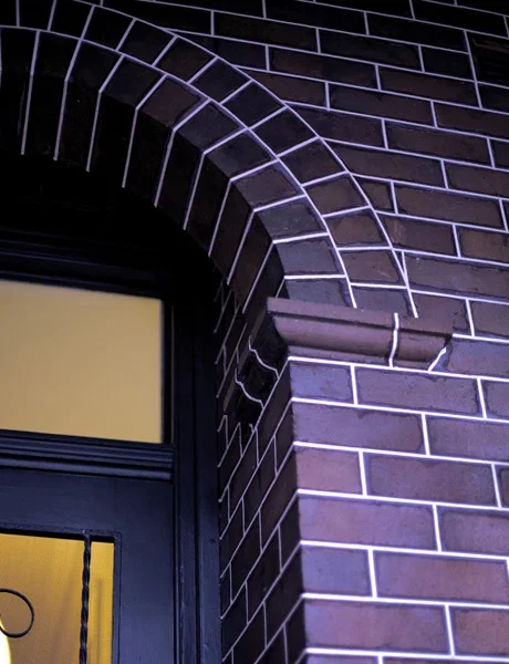 Close-up of a brick building corner with arch and window, lit with purple LED lights.