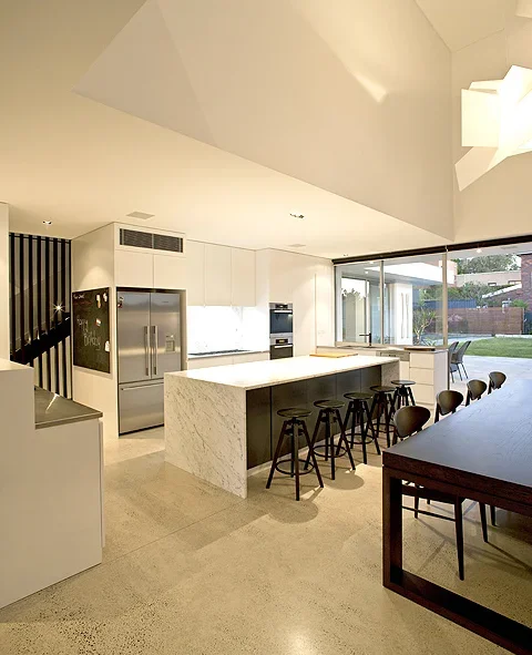 Modern kitchen with white cabinets, marble island, black bar stools, and large glass sliding doors leading to an outdoor patio.