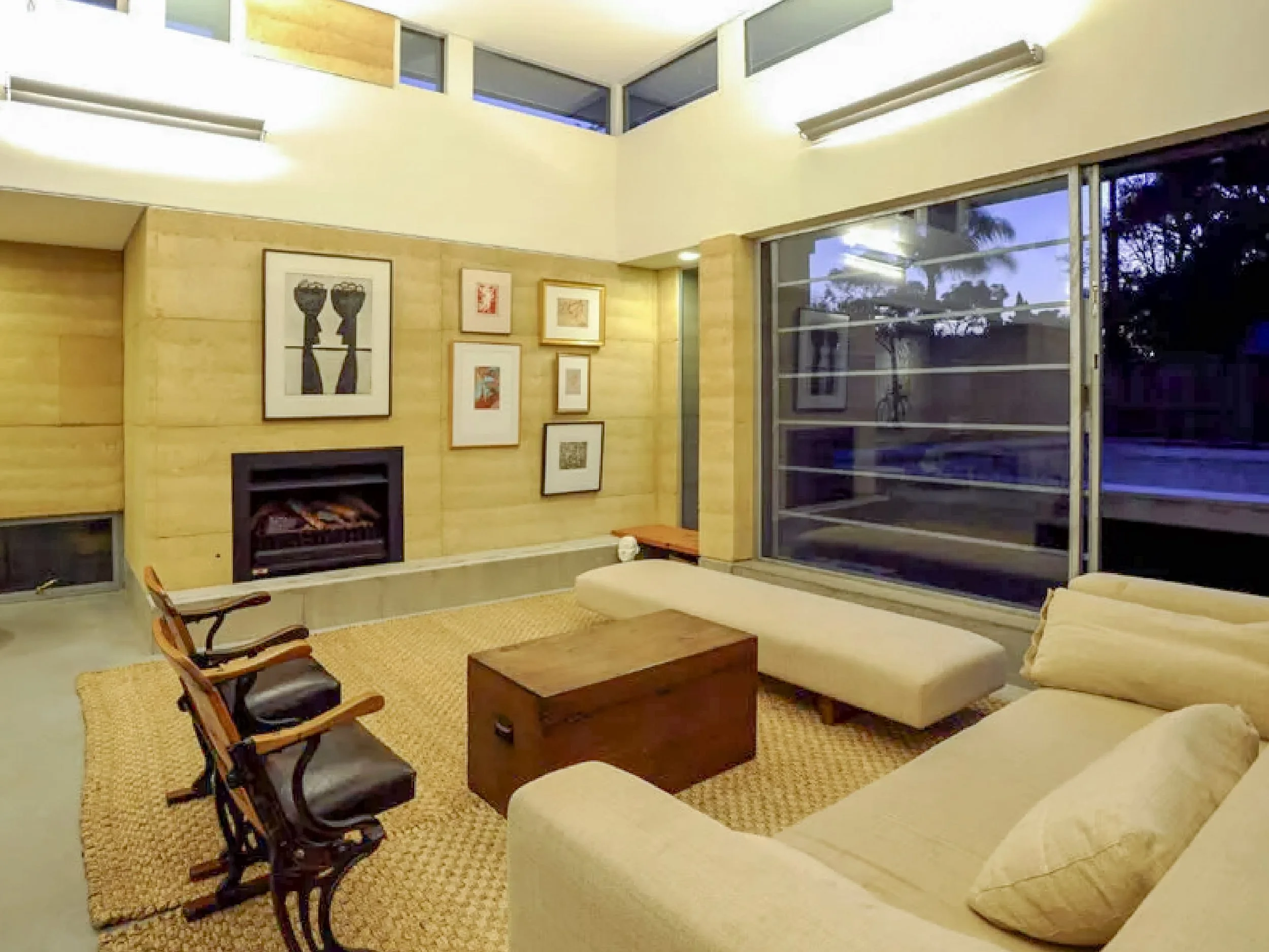 Living room with beige sofas, wooden coffee table, armchair, artwork on the wall, window with blinds, and fireplace.