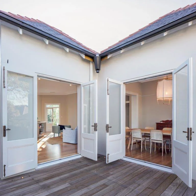View from a balcony showing open double doors leading to a living room and a dining room inside a house.