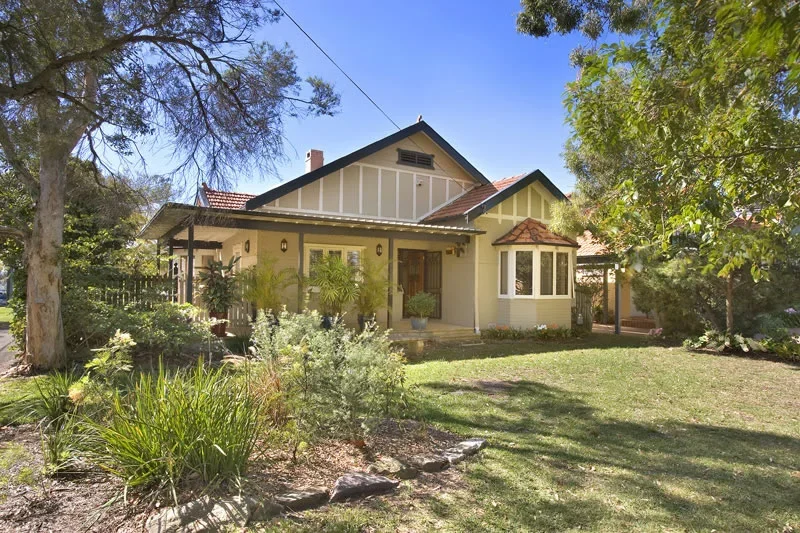 A charming single-family house with a large front yard, surrounded by trees and lush greenery, under a clear blue sky.