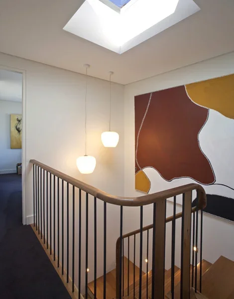 Interior view of a staircase area with a wooden railing, two hanging pendant lights, Abstract wall art, and a skylight in the ceiling.