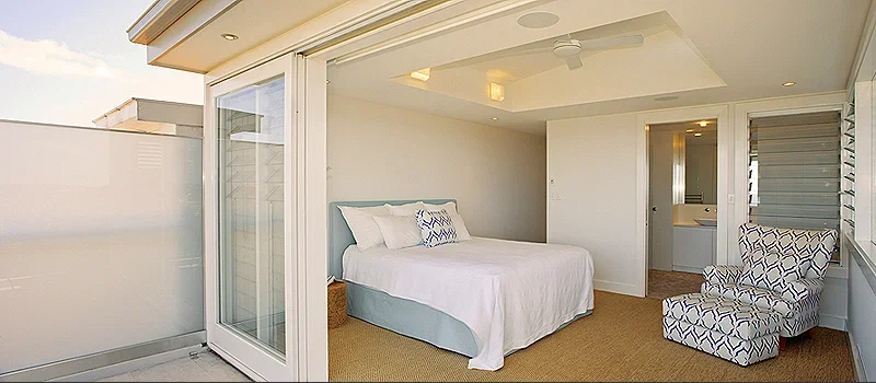Hotel room with a bed, a patterned armchair, and a sliding glass door leading to an outdoor balcony.