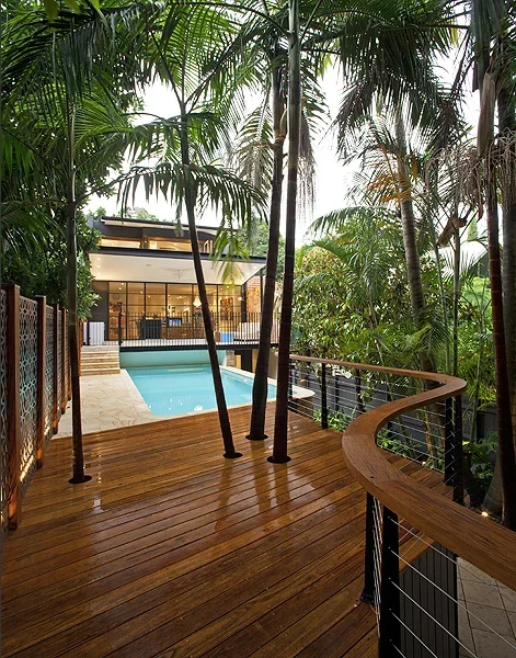 Wooden balcony overlooking a swimming pool surrounded by palm trees in a tropical setting.