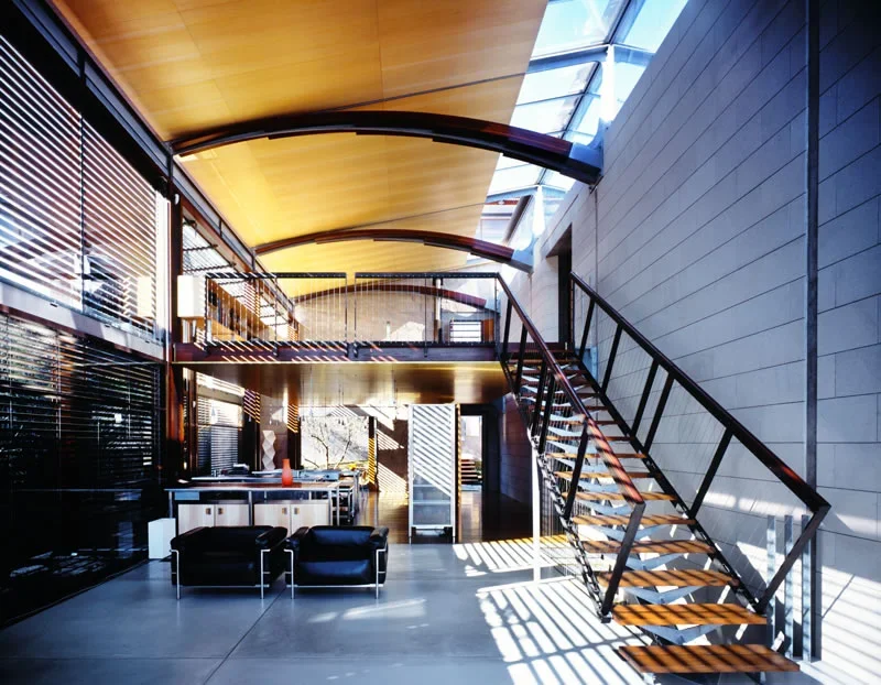 Modern interior with a staircase, seating area, and large windows allowing natural light.