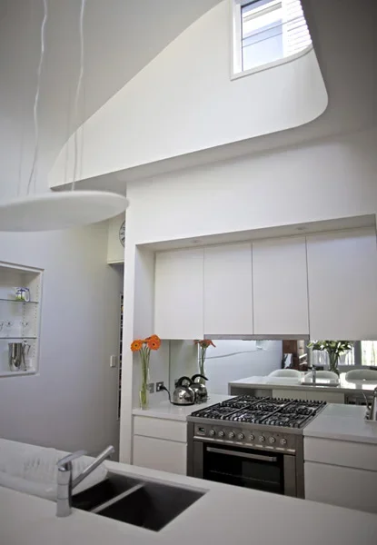 Modern kitchen with white cabinets, stainless steel stove, flowers in vases, and a large mirror reflecting the room.