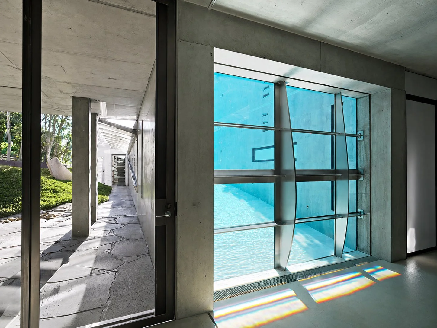 Designed by Peter Stutchbury.  Underwater swimming pool window at Bay House, framed by exposed concrete beside the sheltered garden walkway