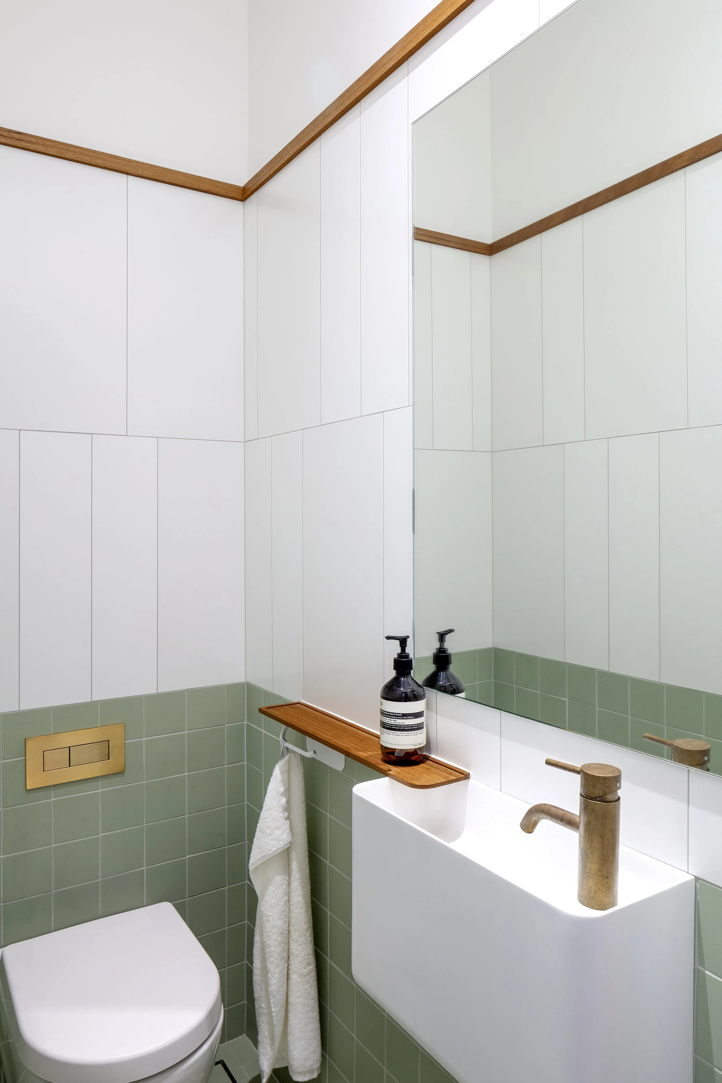 Coogee bathroom with a wall-hung basin, sage-green tiles, timber detailing and a window overlooking greenery.