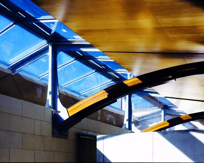 Interior view of a modern building with a wooden ceiling, large windows, and curved architectural elements with black and yellow accents.