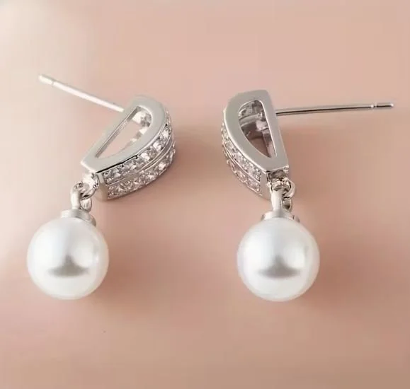 Silver earrings with white pearls and gem accents on a beige background.