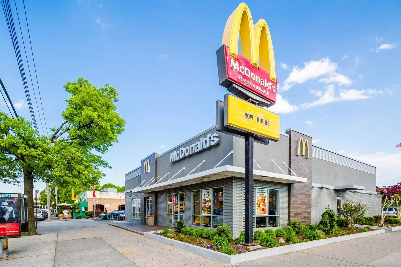 Exterior of a McDonald's restaurant with a large sign, green trees, and clear blue sky.