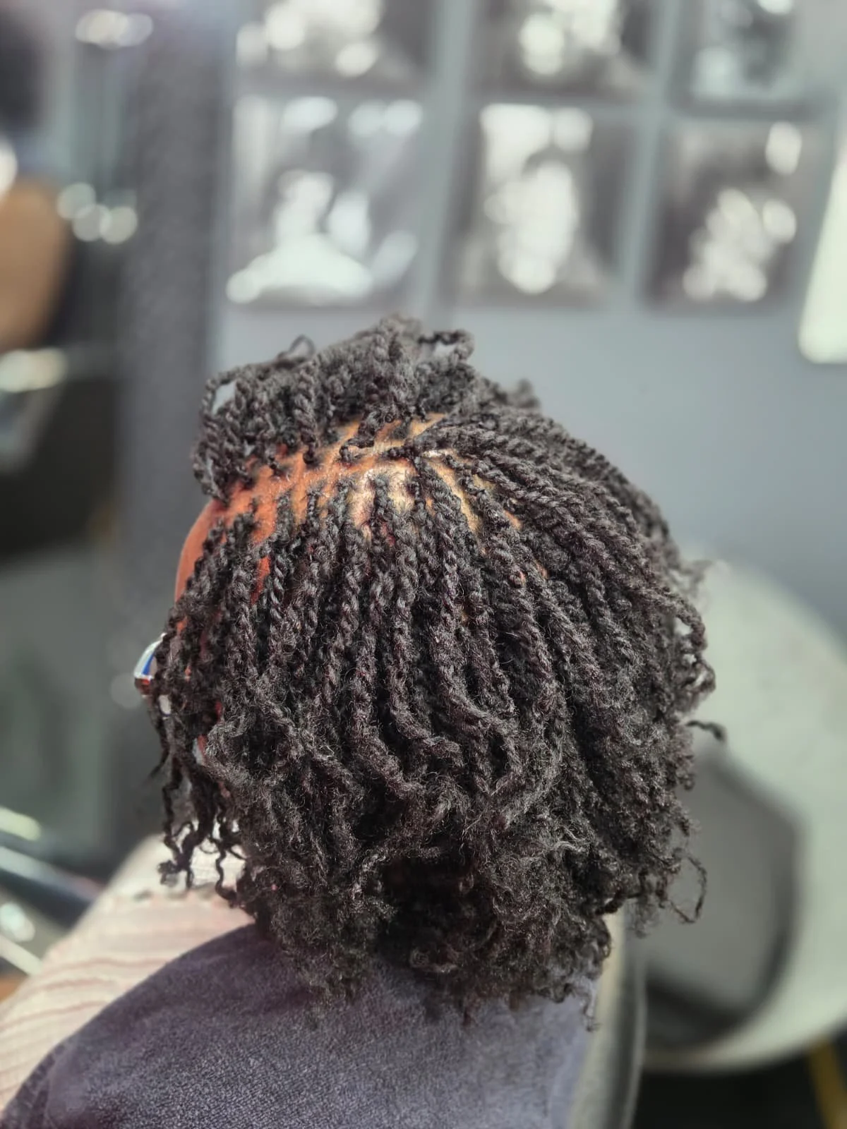 Close-up of a person's head showing freshly styled natural black hair in small twists or locs, with the scalp visible at the crown, taken inside a vehicle with blurred window background.