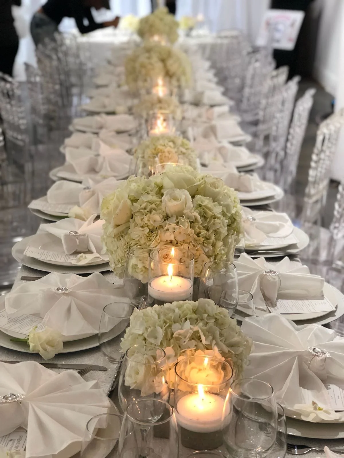 Elegant banquet table set for a wedding or formal event, decorated with white floral arrangements and lit candles.