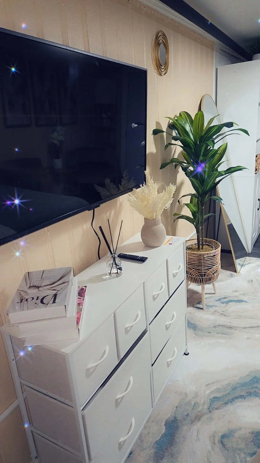 Living room corner with a white dresser, decorative items, a large potted plant, and a wall mirror.