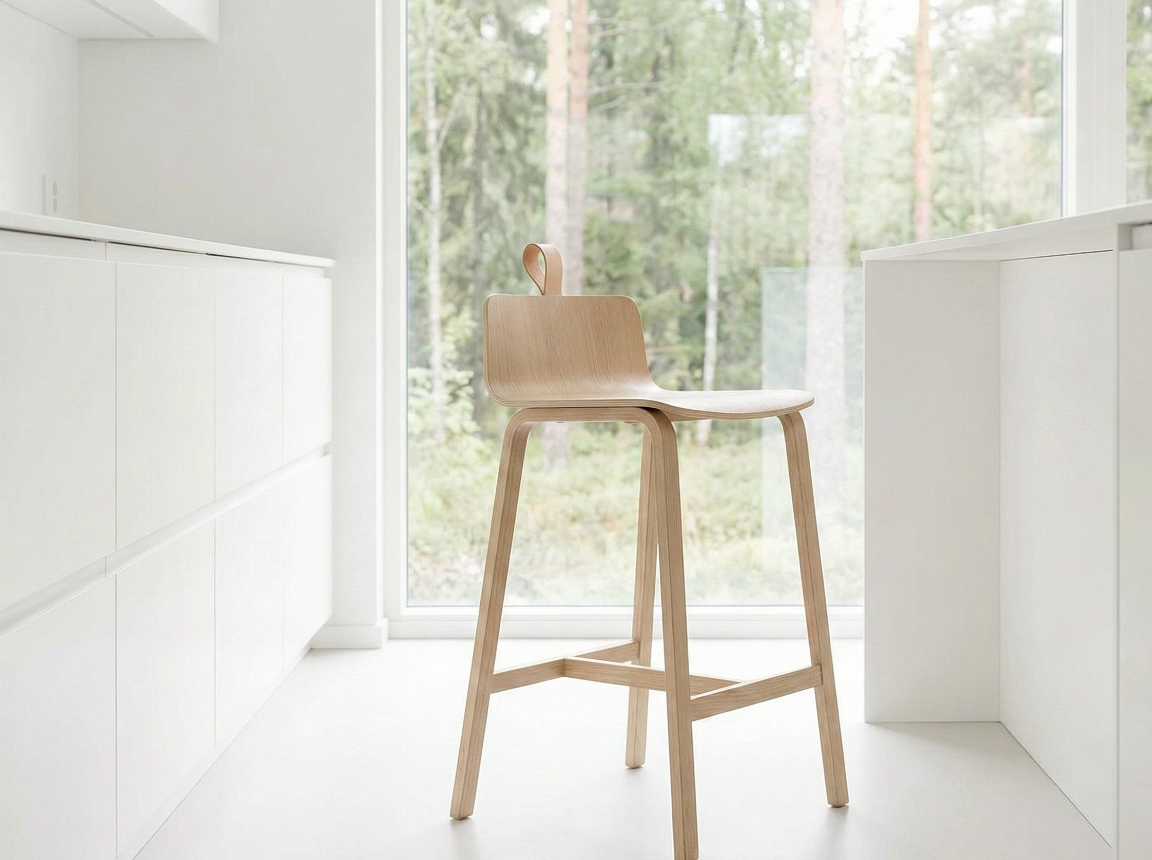 A minimalist kitchen with white cabinetry and a large window overlooking a forest, featuring a single wooden chair with a curved seat and backrest.