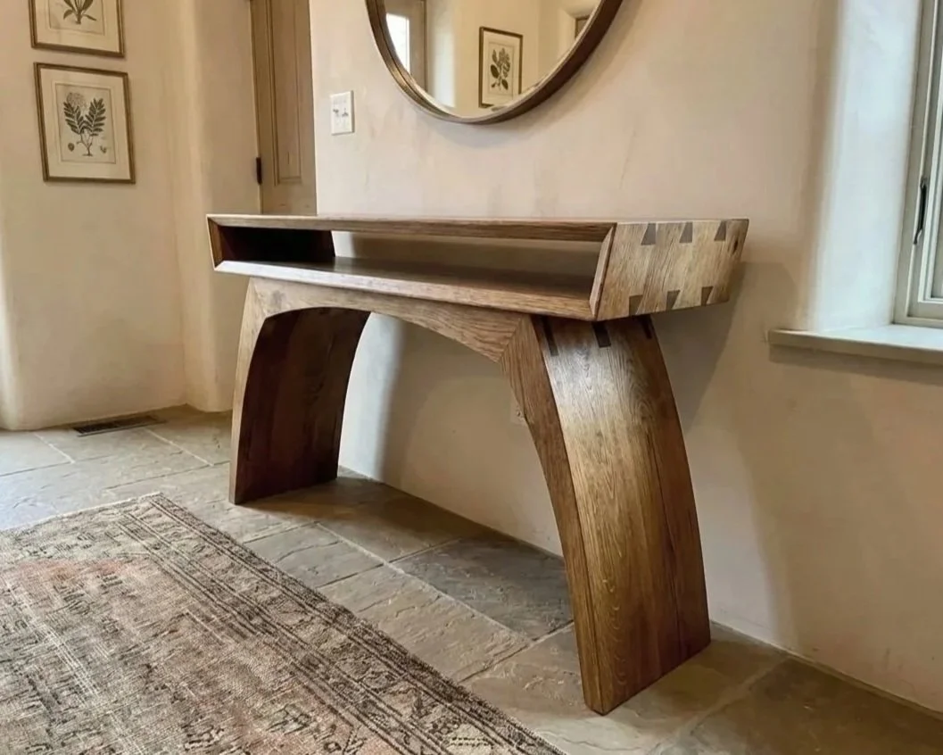 Wooden console table with curved legs in a hallway, above a rug, near a window.