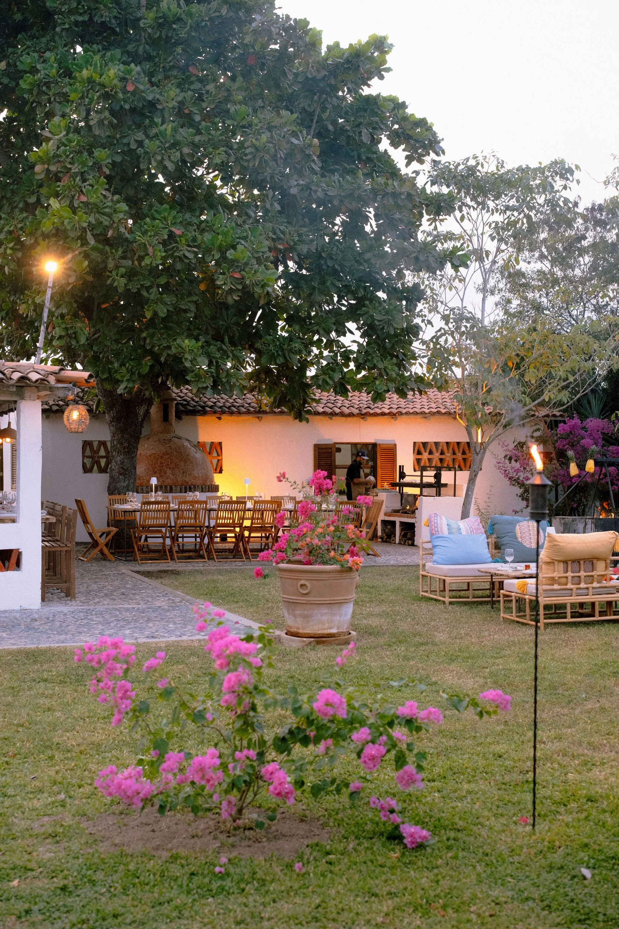 Jardín del restaurante polo careyes decorado para una fiesta al atardecer con mesas, sillas, sillones, flores y una fogata.