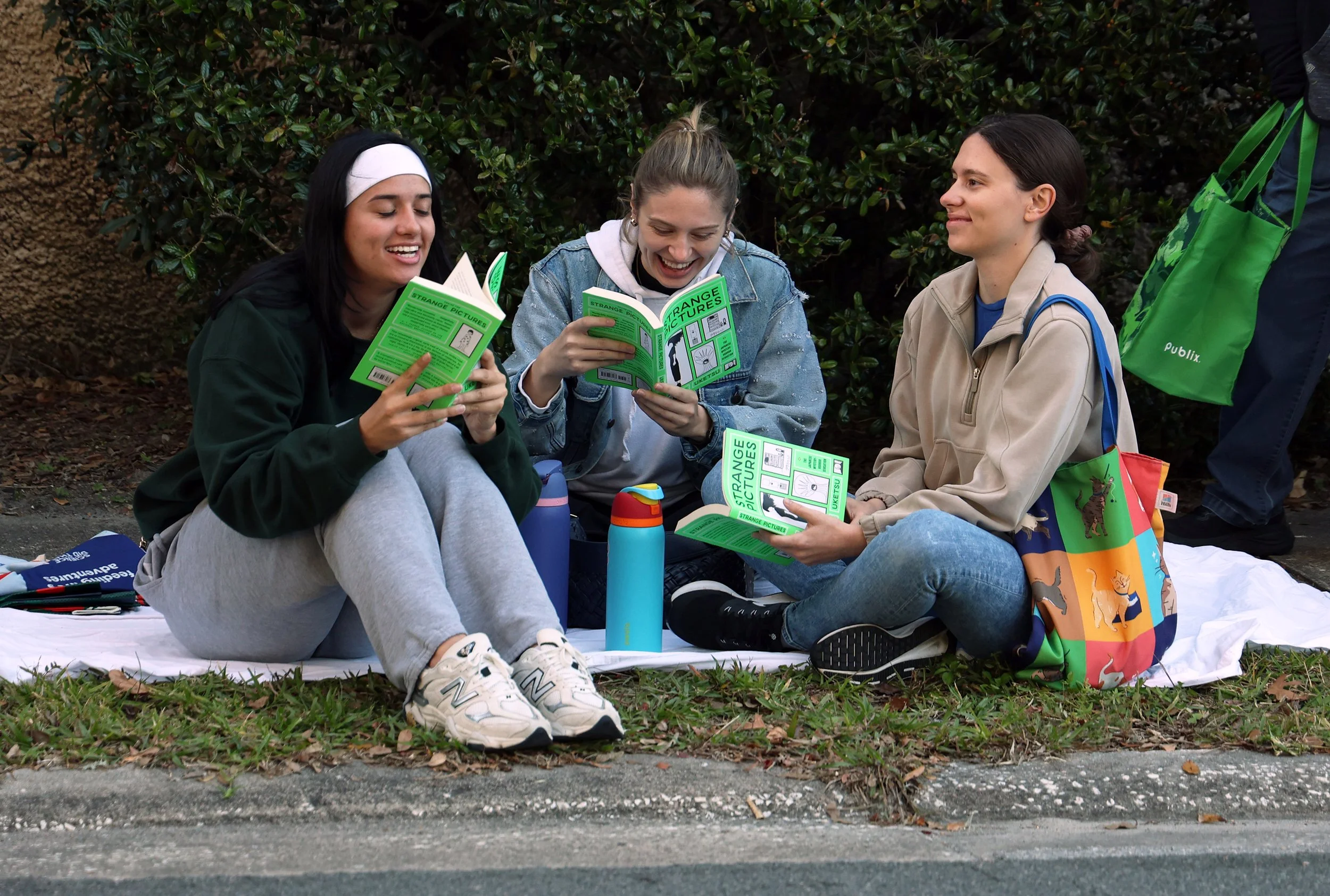Kathryn Morin (left), Samantha Higgins (center), and Lexie Ewing (right) read “Strange Pictures” together as they wait among hundreds of others for the Friends of the Library Fall Book Sale in downtown Gainesville on Saturday, Oct. 25, 2025. 