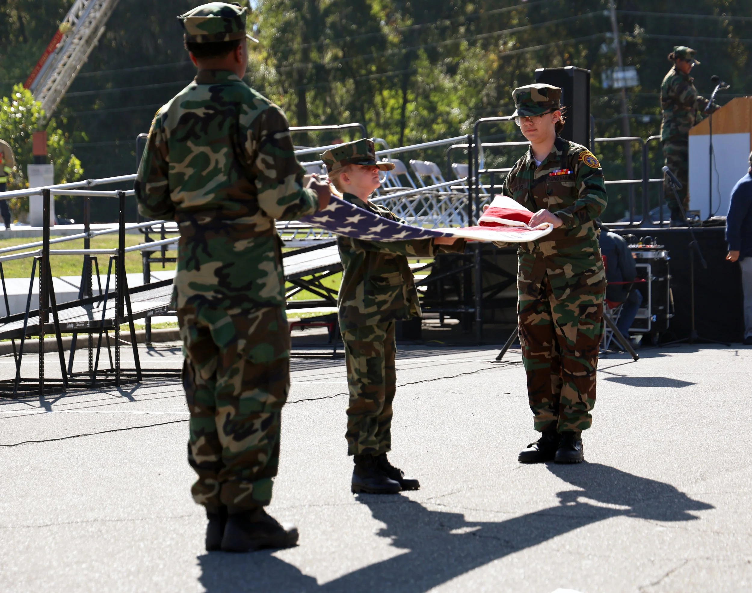 Private First Class Jade Santos (right) folds the American flag as Private Kaydance Lancaster (center) and Private First Class Charles Jones (left), all members of the Young Marines, hold it in place during Alachua County’s Veterans Day celebration a