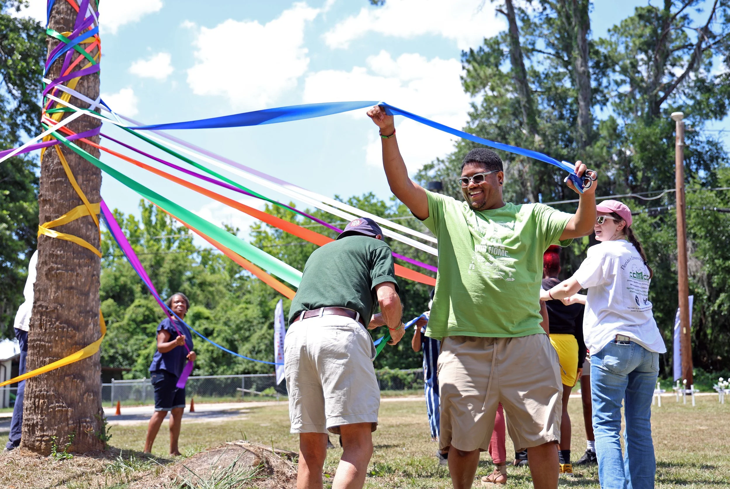 Errol Nelson weaves a blue ribbon around a palm tree maypole alongside 11 others during the Florida Emancipation Celebration at the Cotton Club Museum and Cultural Center in Gainesville, Fla., on May 24, 2025. Each year, attendees join together to pl
