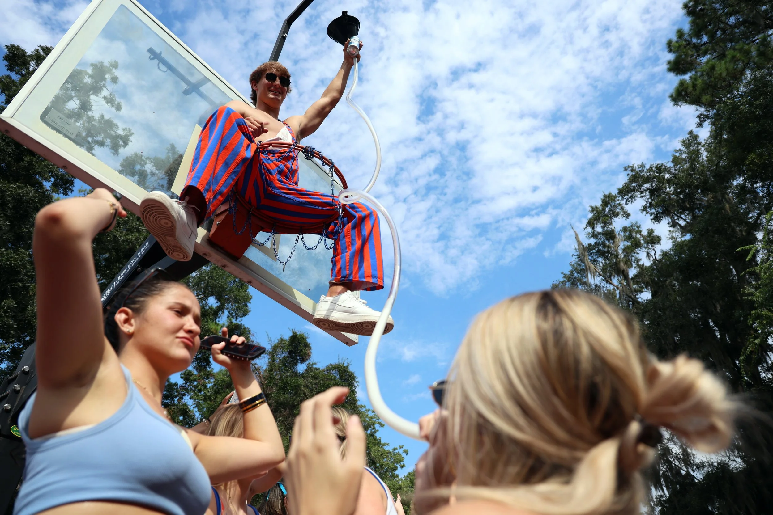 Robby Lizama holds the end of a beer funnel while sitting on top of a basketball hoop at Alpha Epsilon Pi’s tailgate party before the LIU vs. UF game on Saturday, August 30, 2025.