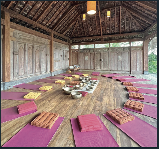 Indoor yoga or meditation space with purple mats and folded cushions arranged around a wooden table with singing bowls.