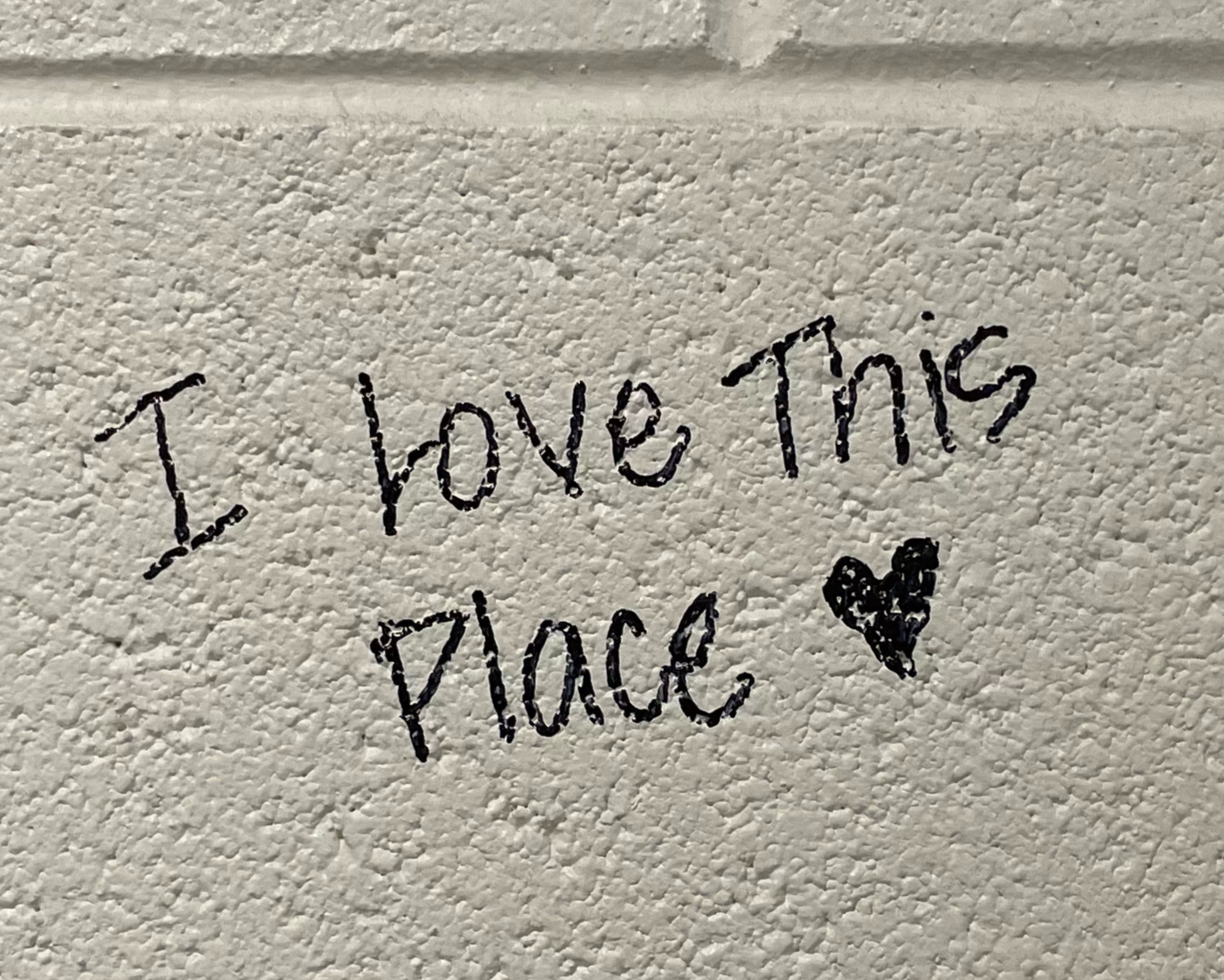 Handwritten message on a textured white wall that says, 'I love this place' with a small heart drawing.