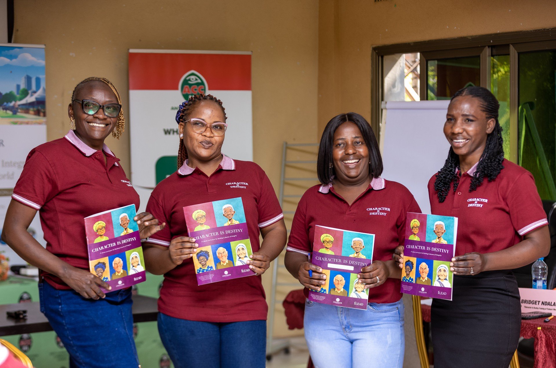 Four women in red shirts holding books titled "Character is Destiny," standing indoors at a presentation or event.