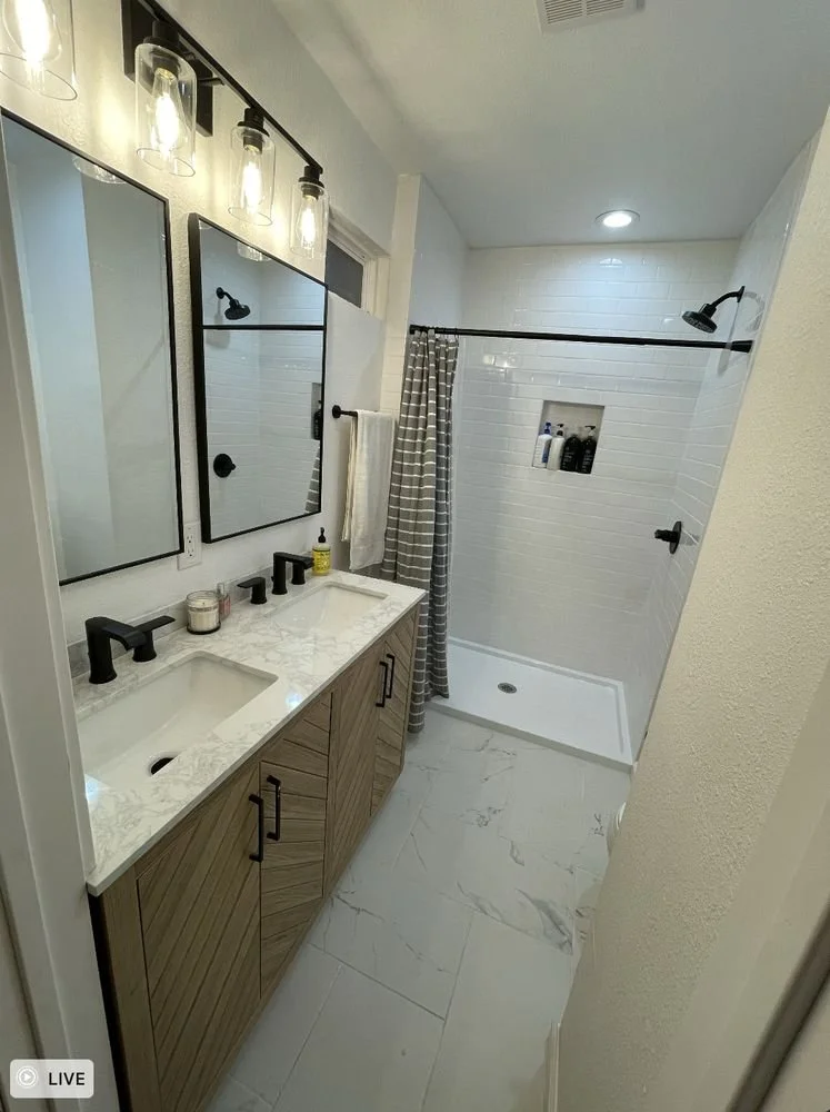 Modern bathroom with dual sinks, a wooden vanity, and a walk-in shower with white subway tile walls and a shower niche holding toiletries.