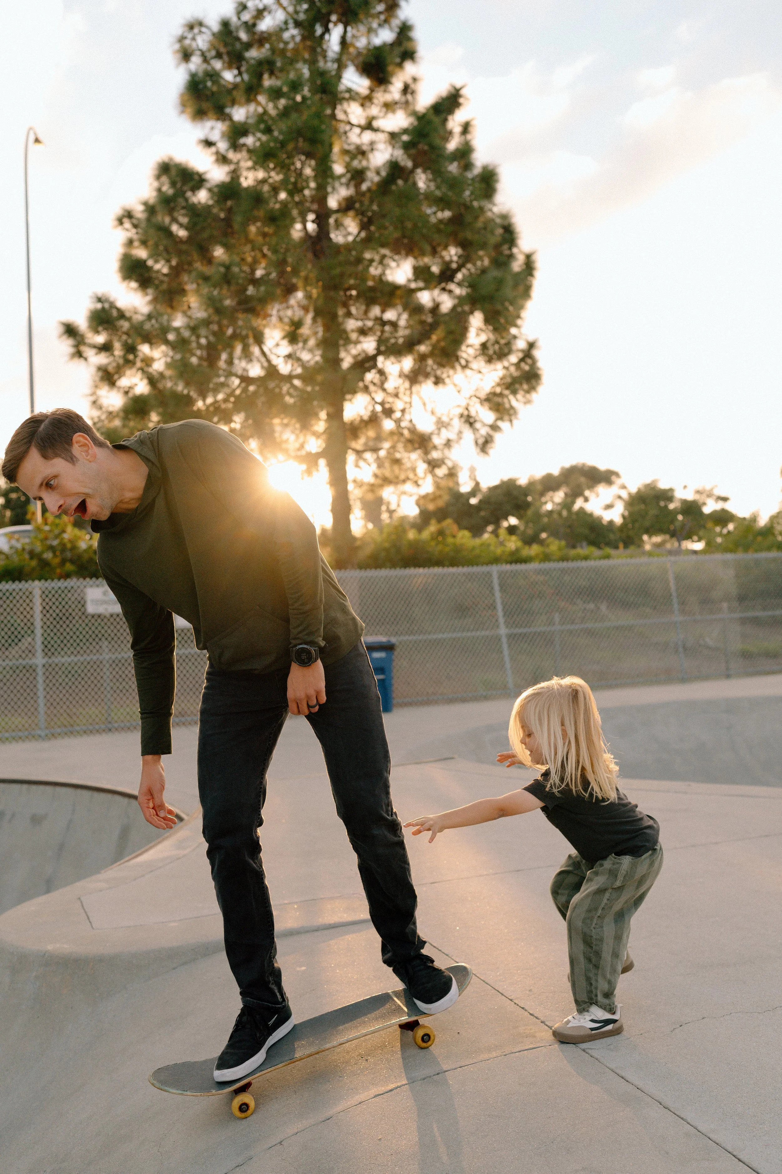 A man skateboarding at a skate park being pushed by a young girl during sunset.