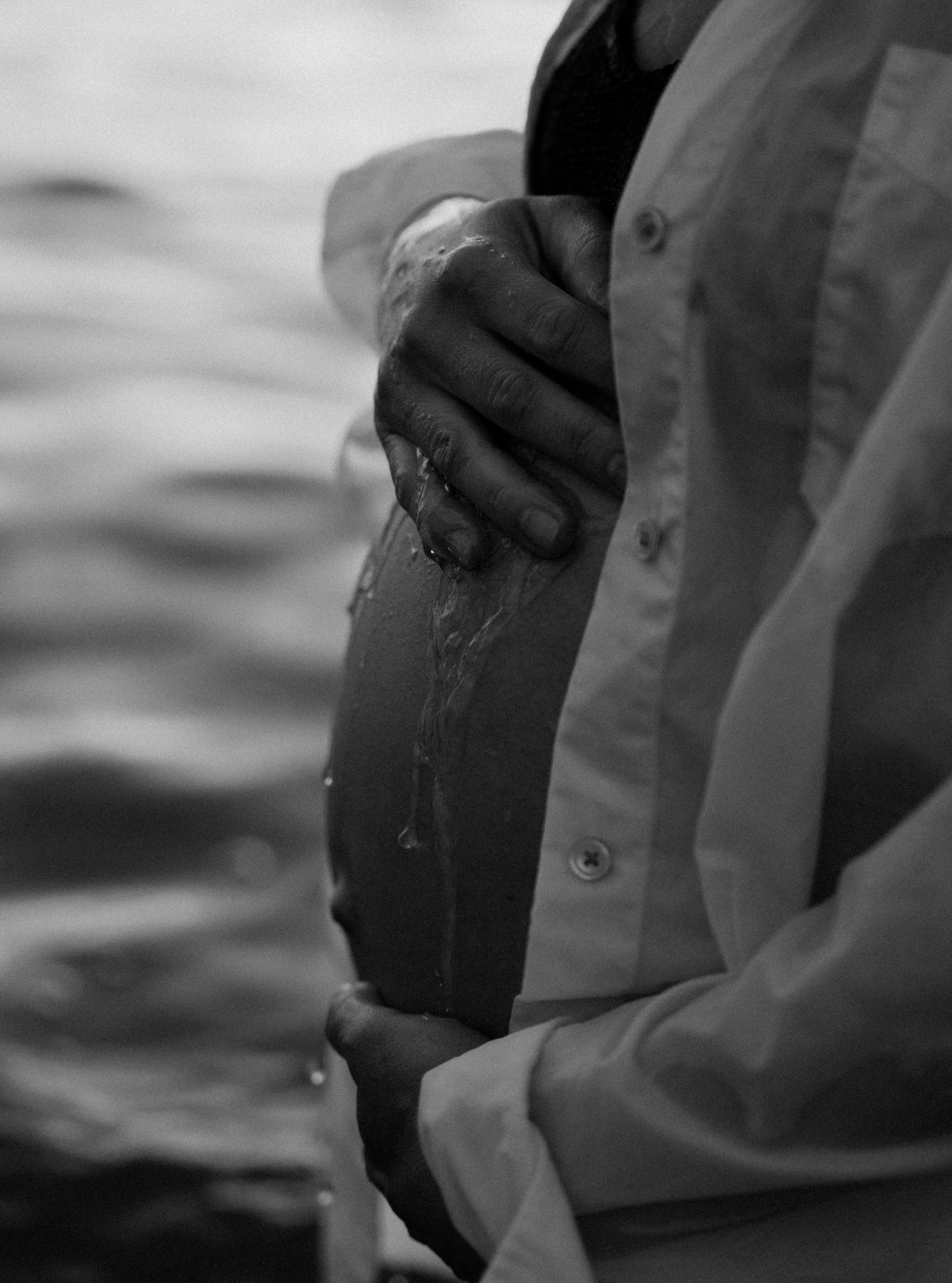 A person holding a rock with water dripping from it near a body of water.