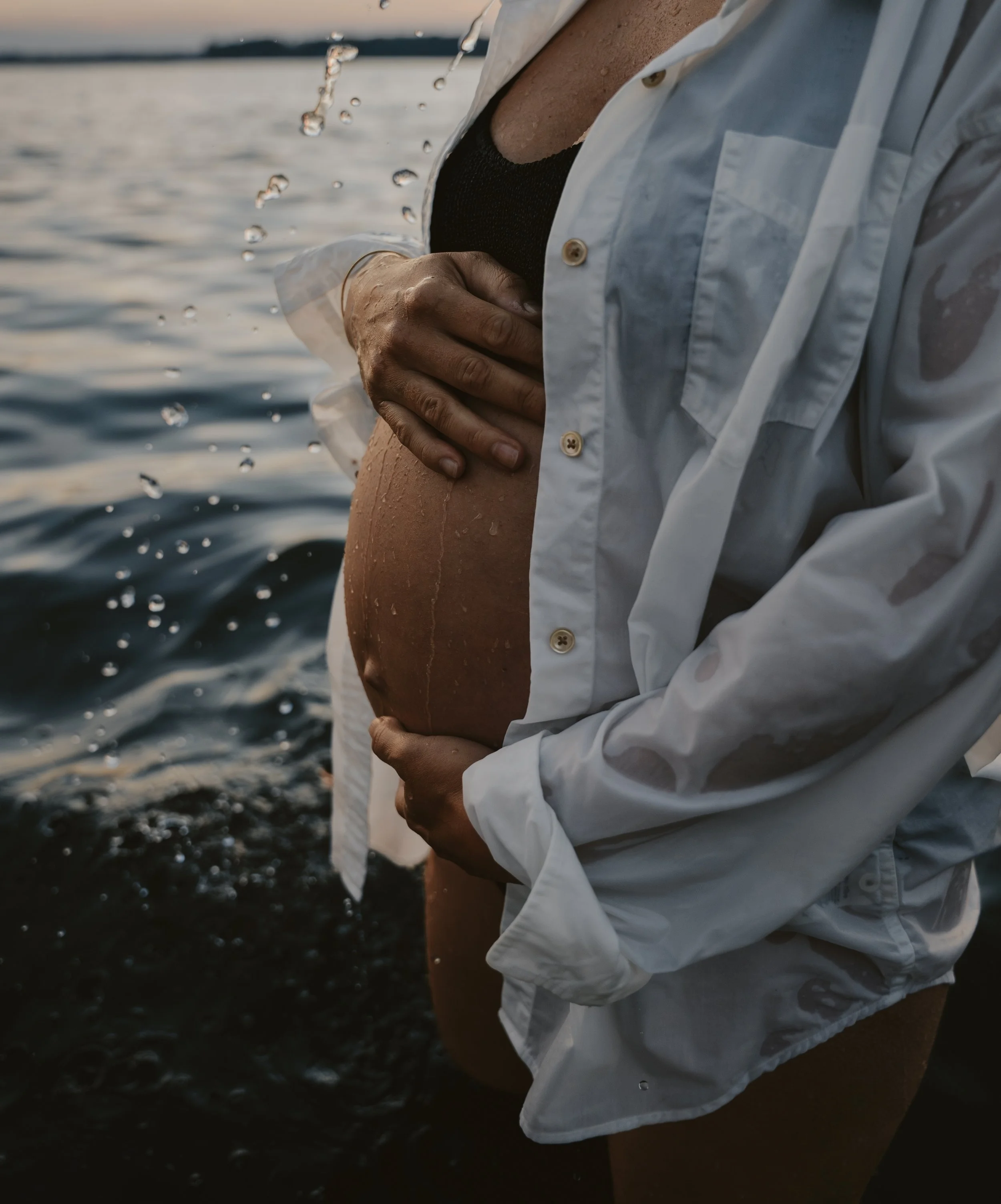 Person in a white shirt standing in water, holding their pregnant belly.