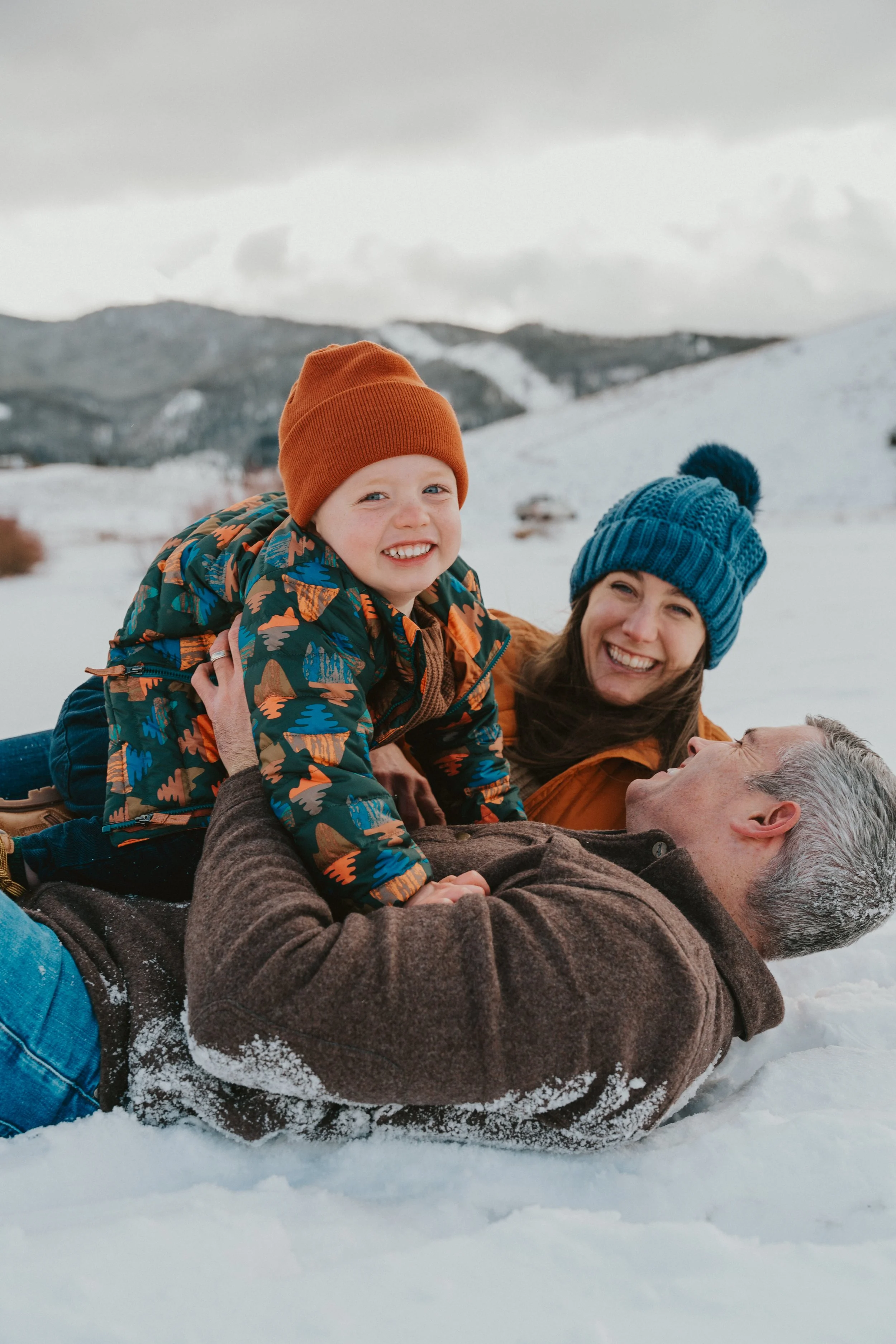 Family enjoying snow on a mountain hillside, lying on the snow with winter clothing, smiling.