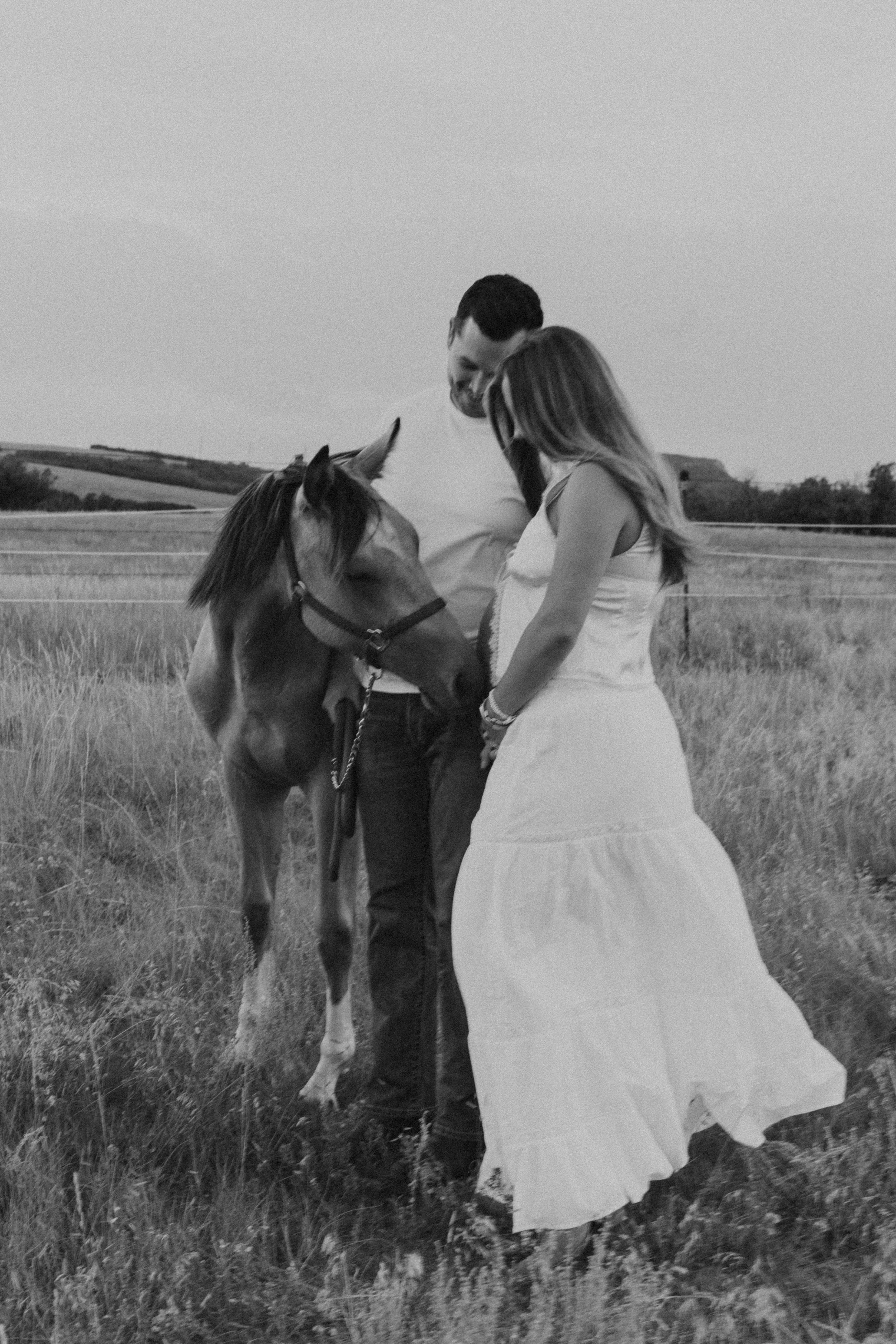 A couple with a horse in a grassy field, black and white photograph.