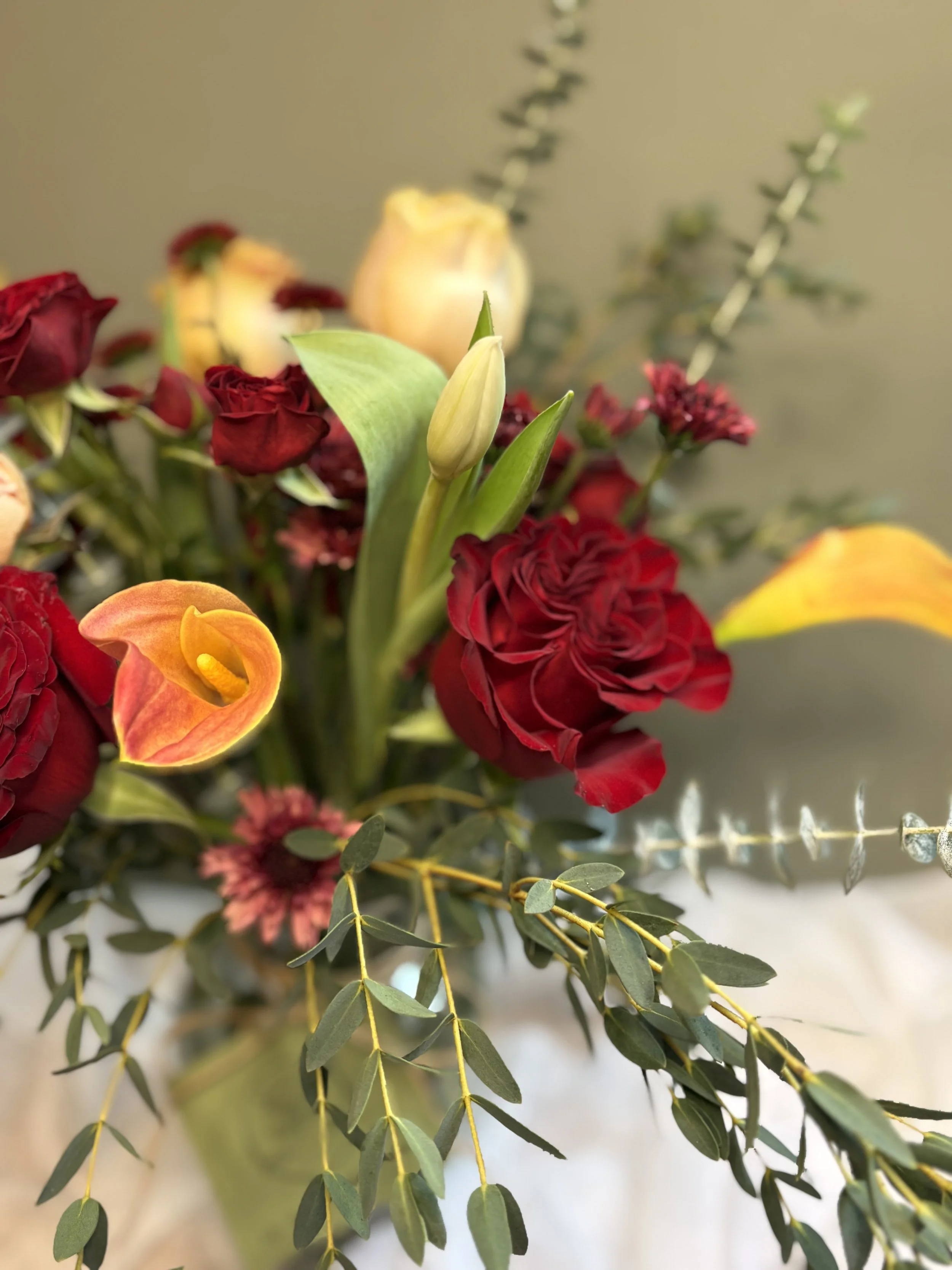 A close-up of a flower arrangement with red, yellow, and white flowers and green foliage.