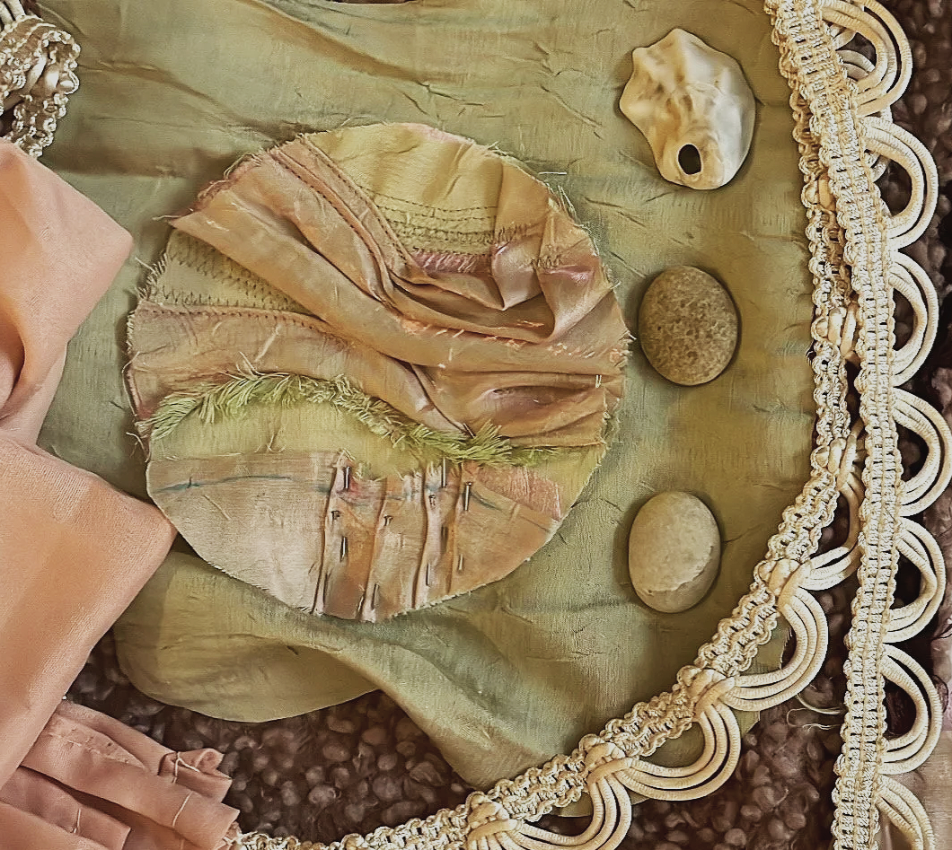 A collection of stones, seashells, and a fabric circle with a green feather, arranged on a green fabric with decorative trim.