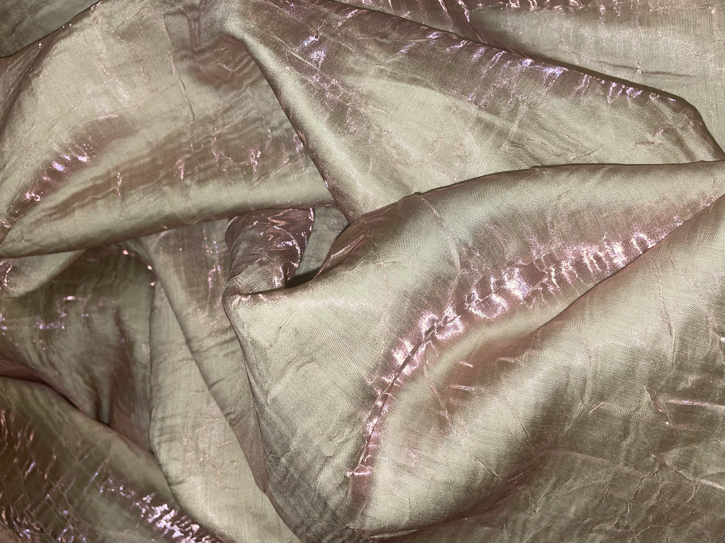 Close-up of a shiny, beige fabric with pink accents, showing folds and a reflective, crinkled texture.