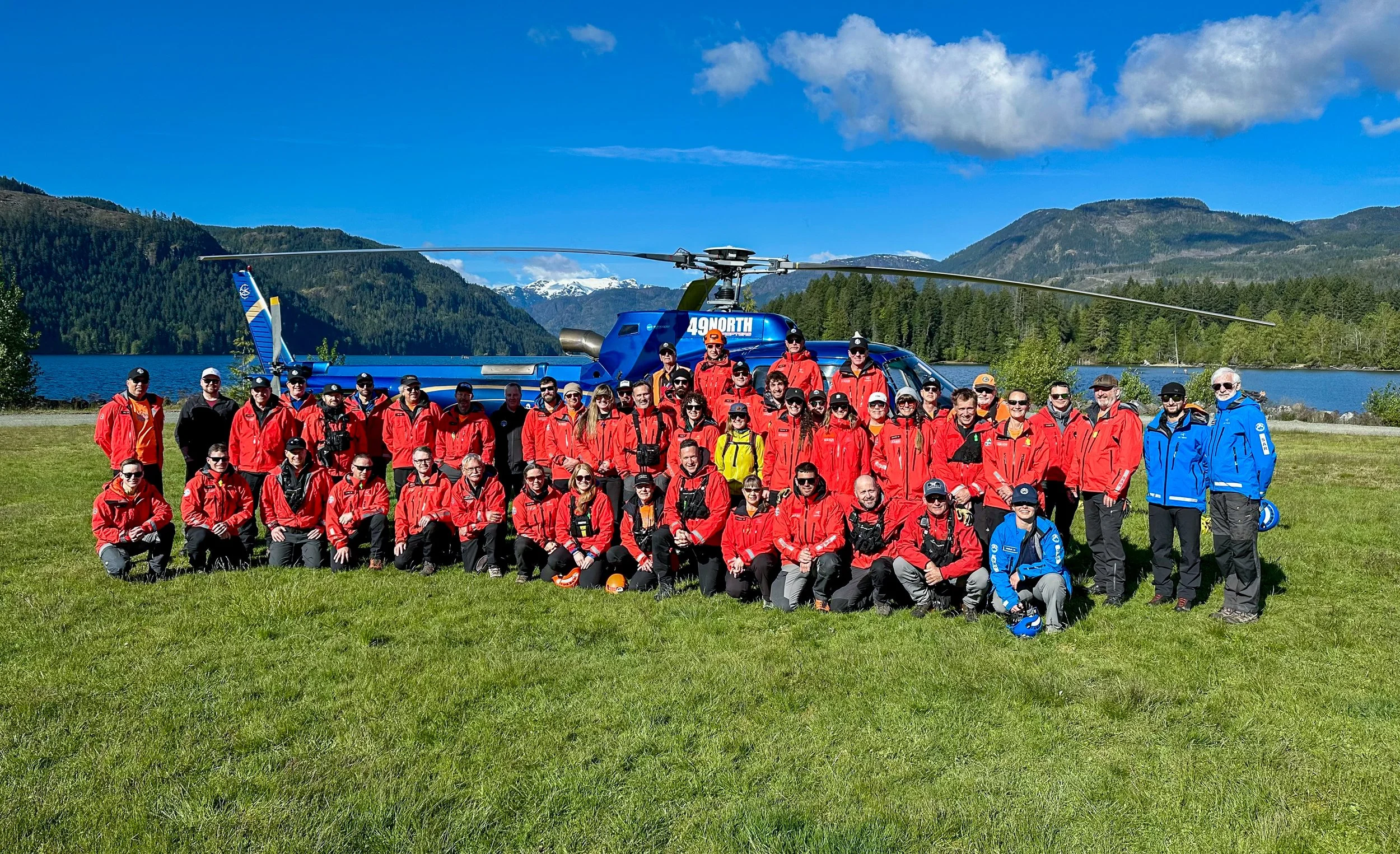 Comox Valley Search & Rescue team in red and blue jackets posing in front of a helicopter at Comox Lake.