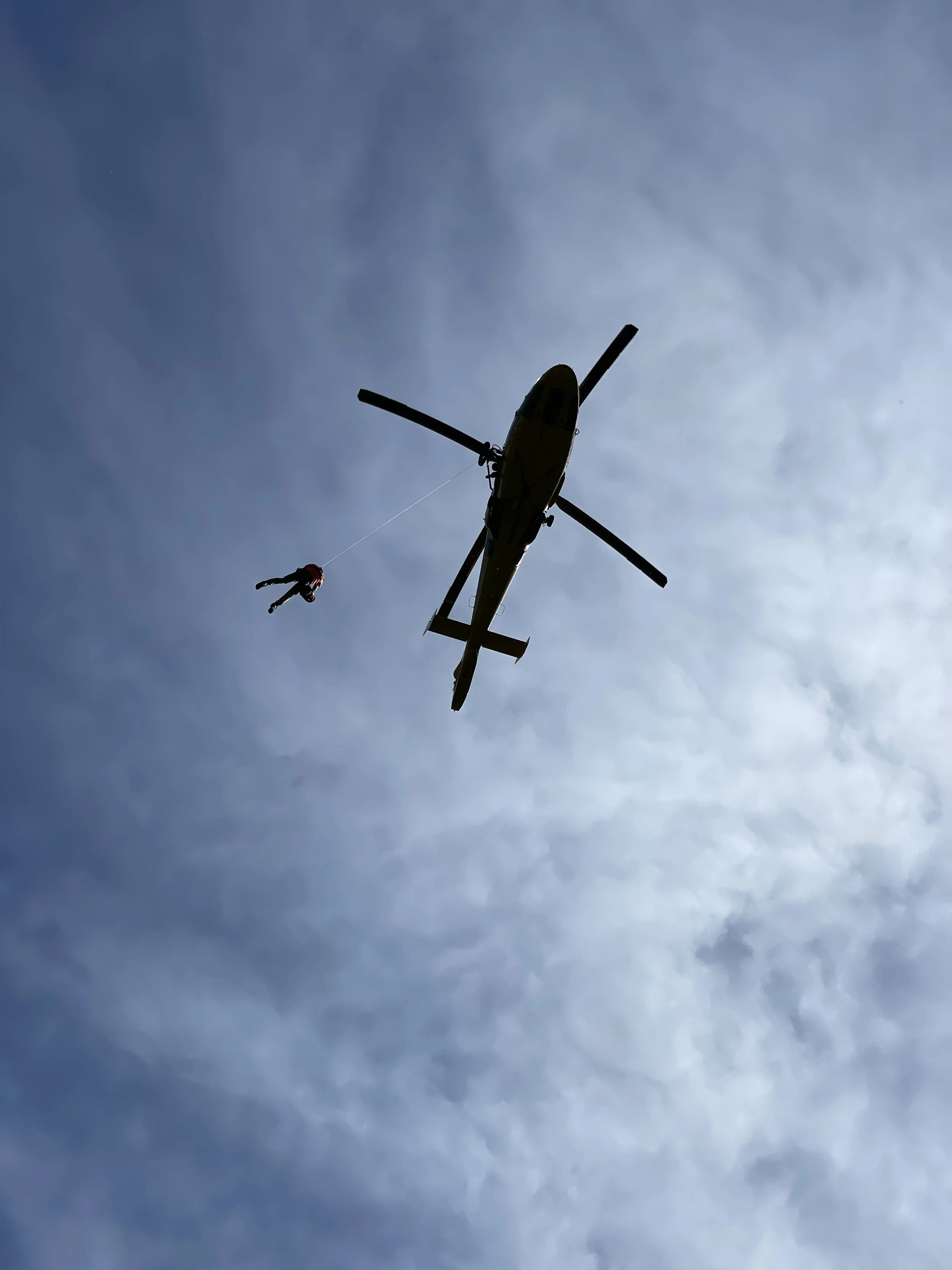 A helicopter flying in the sky with a person rappelling down from it during the daytime.