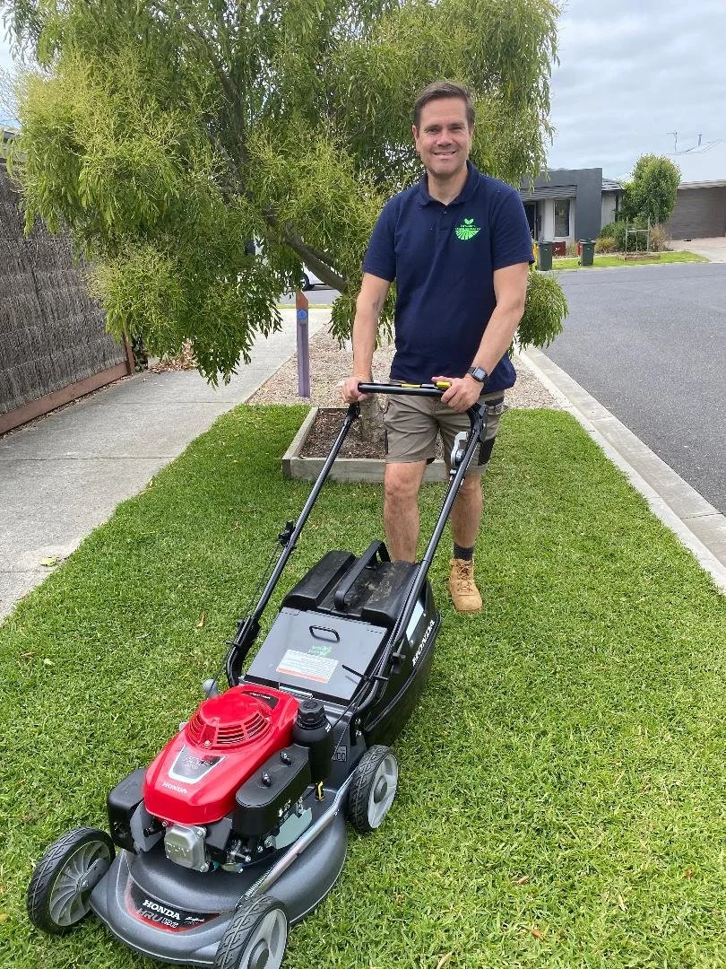 A man smiling while mowing the lawn with a gas-powered lawn mower.