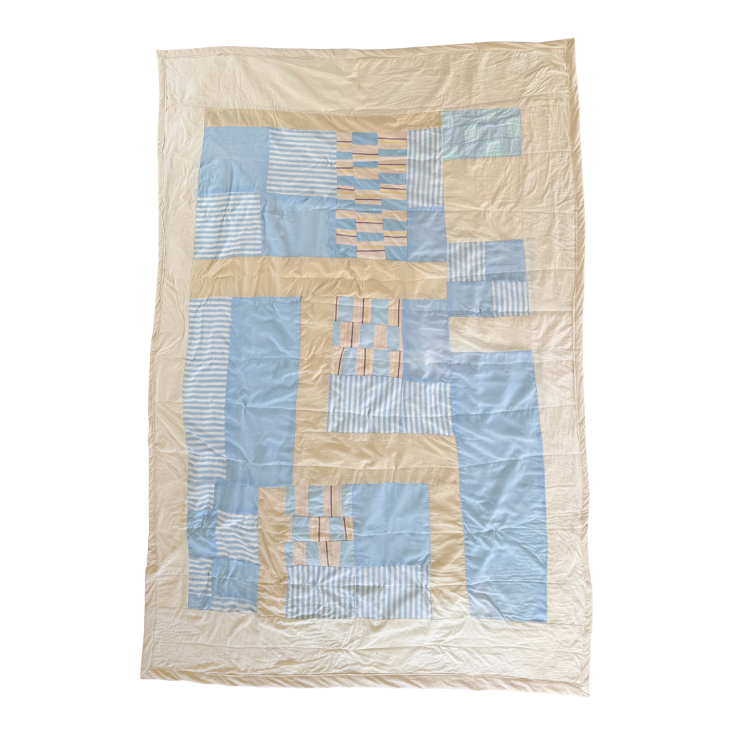 A quilt with geometric patterns in blue, beige, and striped fabric laid flat on a surface.
